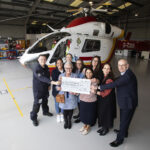 Priti Patel MP presents a donation cheque to Essex & Herts Air Ambulance Trust alongside Mrs Sue Miller, the wife of the late Dennis Miller and his three daughters Sarah, Claire and Lisa. They are joined by EHAAT Chief Executive Jane Gurney, Aviation & Operations Director Paul Curtis and members of the emergency response team at Earls Colne airbase.